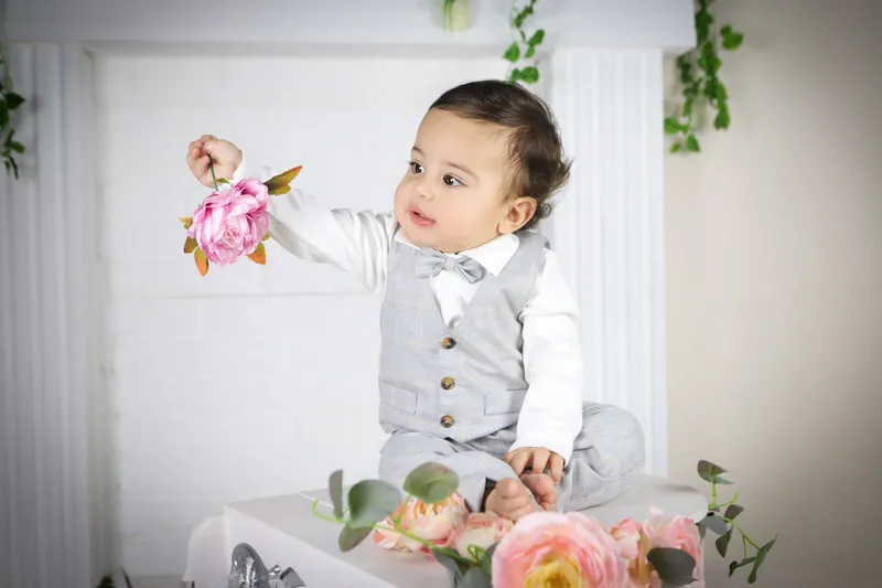 Gri kareli yelek ve papyonuyla çiçek tutan şık 1 yaş bebek
