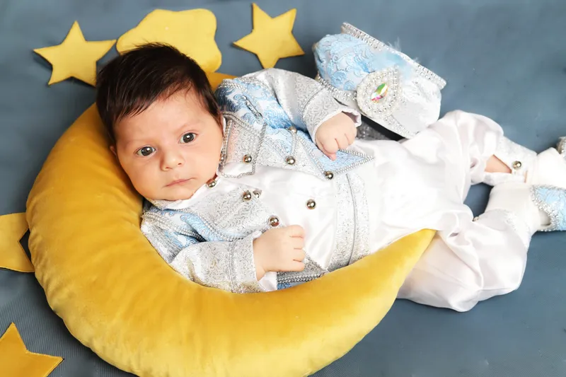 Sarı hilal yastık üzerinde sünnet kıyafeti ve fesiyle yatan minik bebek